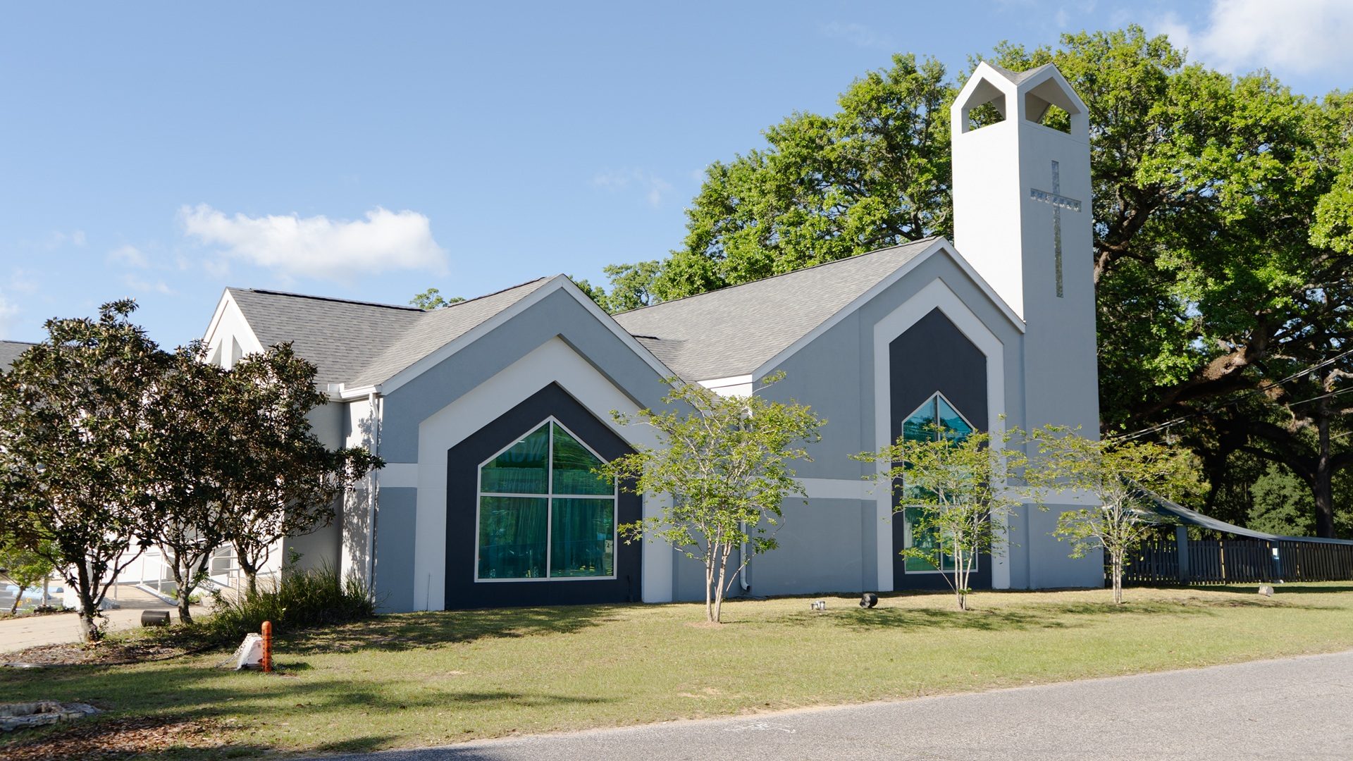 Exterior of St. Andrew Orthodox Church Pensacola, bell tower with iron cross, arched stained-glass windows, palm trees